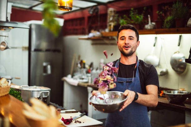 Portrait of a handsome, positive chef cook grinning in the vibrant restaurant kitchen, expertly drizzling chutney over Mumbai’s iconic pav bhaji with infectious street food passion!